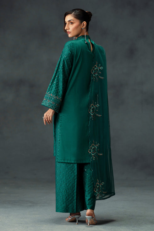 Woman wearing a teal embroidered outfit against a gray background